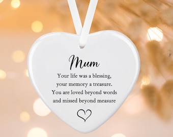 May include: A white heart-shaped ceramic ornament hanging from a white ribbon. The text reads: Mum, Your life was a blessing, your memory a treasure. You are loved beyond words and missed beyond measure, with a small black heart icon at the bottom.