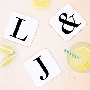 May include: Three white square coasters with black letters. The coasters spell out "L & J".