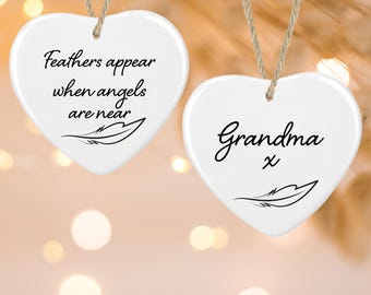 May include: Two white heart-shaped ceramic ornaments hanging from jute twine. The left ornament features the black text "Feathers appear when angels are near" with a feather graphic. The right ornament features the black text "Grandma x" with a feather graphic.