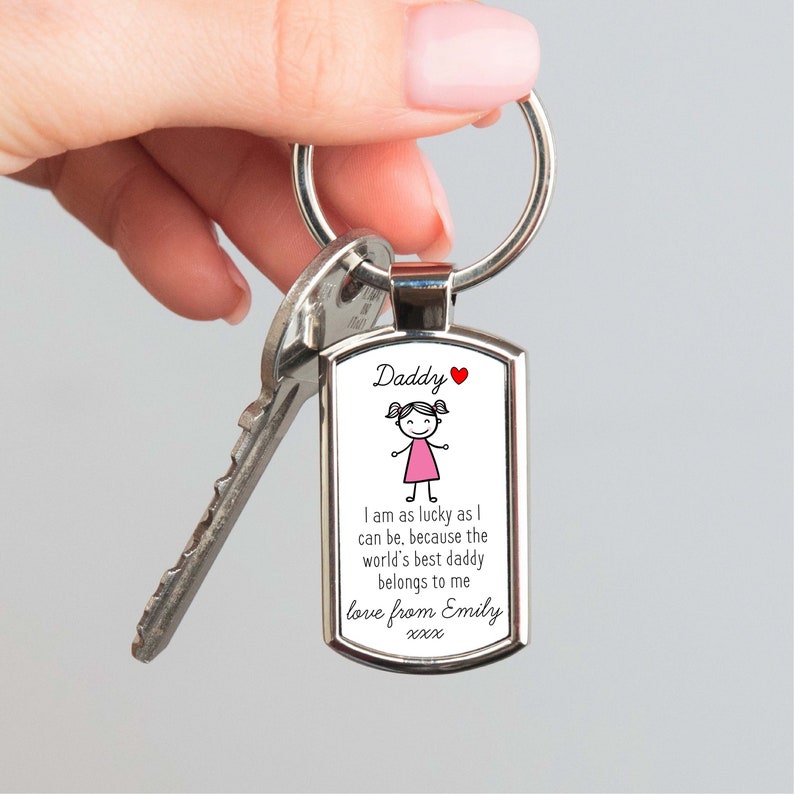 A high-quality metal keyring with a silver finish, personalized with a 'Love Daddy from Daughter' message. The front features a cute hand-drawn stick figure girl in a pink dress and the sentimental quote "I am as lucky as I can be, because the world's best daddy belongs to me love from Emily". Perfect birthday or Christmas gift for a dad from his daughter.