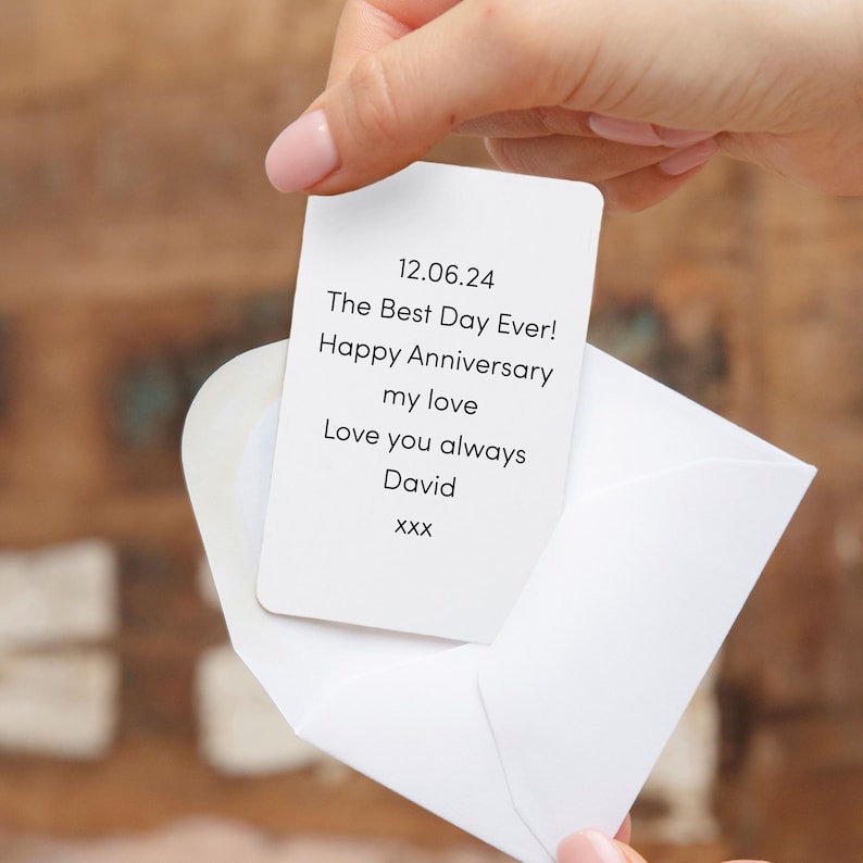 Pu&ograve; includere: Una carta bianca con angoli arrotondati viene tenuta, mostrando il testo "12.06.24 The Best Day Ever! Happy Anniversary my love Love you always David xxx" in nero. La carta &egrave; parzialmente all'interno di una busta bianca.
