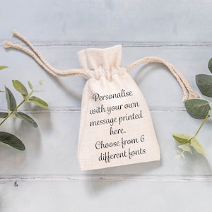 May include: A small, off-white, drawstring bag made of natural fabric with the text "Personalise with your own message printed here. Choose from 6 different fonts" printed on the front.