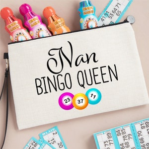 May include: A beige canvas zippered pouch with the words "Nan BINGO QUEEN" in black. The pouch has colorful bingo markers and bingo cards. The numbers 23, 37, and 77 are on the pouch.
