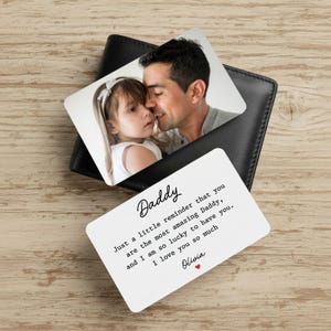 May include: A black leather wallet with two white cards featuring a photo of a father and child. One card has the word "Daddy" and a message: "Just a little reminder that you are the most amazing Daddy..."