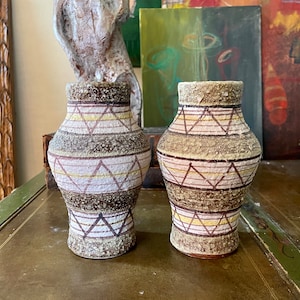 May include: Two ceramic vases with a geometric pattern in shades of brown, white, and yellow. The vases have a textured surface and a slightly flared opening.