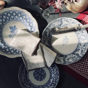 May include: A table setting with three blue and white patterned ceramic plates, two white linen napkins, a silver fork, and a glass of red wine. The plates have a floral design and are arranged on a dark gray surface.