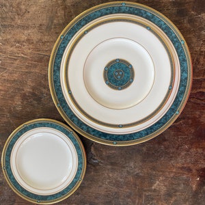 May include: Two ceramic plates with a green and gold design. The larger plate has a smaller plate inside it. Both plates have a white center.