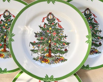 May include: White ceramic plates with a green border and a Christmas tree design. The tree is decorated with ornaments and topped with a candle. Green bow accents are placed around the rim.