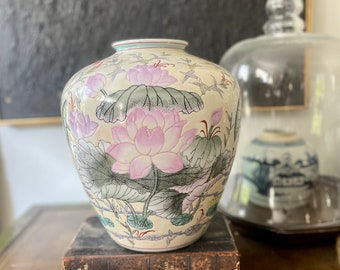 May include: A white ceramic vase with a floral design featuring pink and green lotus flowers. The vase has a round body and a narrow neck.
