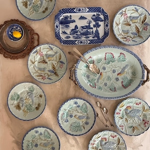 May include: An assortment of decorative plates and serving dishes. The plates feature bird and grape designs in shades of blue, green, and gold. A rectangular blue and white dish and a silver serving tray are also included.