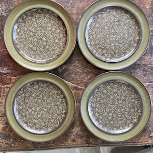May include: Set of four brown and green ceramic plates with a floral pattern. The plates have a raised rim and a slightly textured surface.