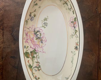 May include: Oval serving dish with a cream-colored interior and a white border. The dish is decorated with a large pink and purple floral design and smaller floral accents. A thin gold line trims the inner edge.