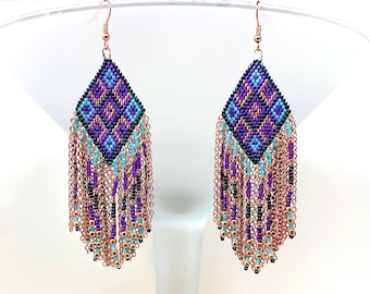 May include: A pair of handmade beaded earrings with a geometric diamond pattern in purple, blue, and black. The earrings have copper-colored chain fringe with turquoise, purple, and gold beads. The earrings hang from copper-colored ear wires.