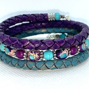 May include: A set of three braided leather bracelets with turquoise and purple beads. The bracelets are layered on top of each other, with the purple leather bracelet on top.