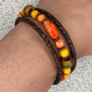 May include: A brown leather bracelet with multiple strands and colorful beads. The beads are orange, yellow, and brown.