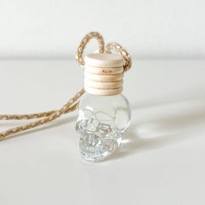 Peut inclure: Une bouteille en verre transparente en forme de crâne avec un couvercle en bois. La bouteille est suspendue à une corde beige et dorée.