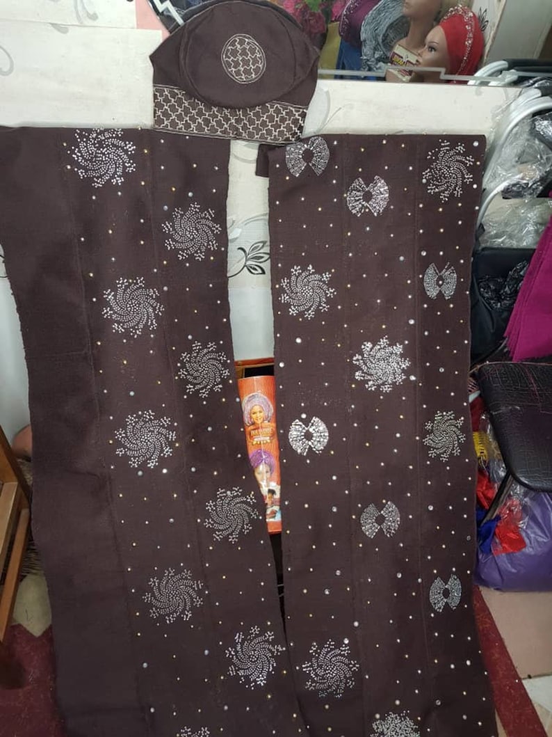 Puede incluir: Un conjunto de tela marr&oacute;n con detalles plateados. El conjunto incluye un tocado y dos paneles largos, cada uno adornado con dise&ntilde;os en espiral y en forma de lazo. Peque&ntilde;os acentos plateados salpican la tela.