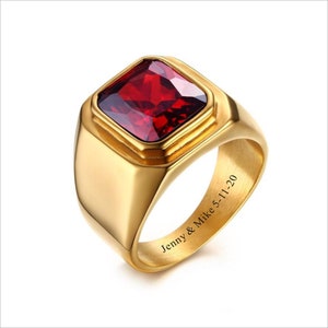 May include: A gold ring with a red square-shaped gemstone. The inside of the band is engraved with "Jenny & Mike 5-11-20".