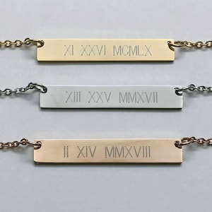 May include: Three gold bar necklaces with Roman numeral dates engraved on them. The top necklace has the date "XI XXVI MCMLX", the middle necklace has the date "XIII XXV MMXVII", and the bottom necklace has the date "II XIV MMXVIII".