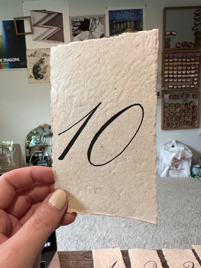 May include: A beige paper table number with the number 10 written in black ink.