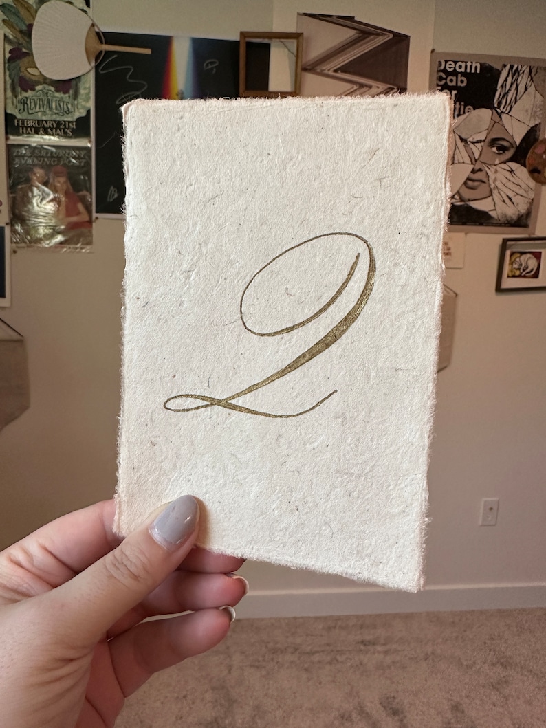 May include: A white card with a gold number "2" written in cursive script.