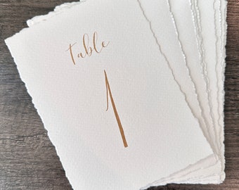 Números de mesa de boda hechos a mano con bordes desbarbados, caligrafía sobre papel texturizado.