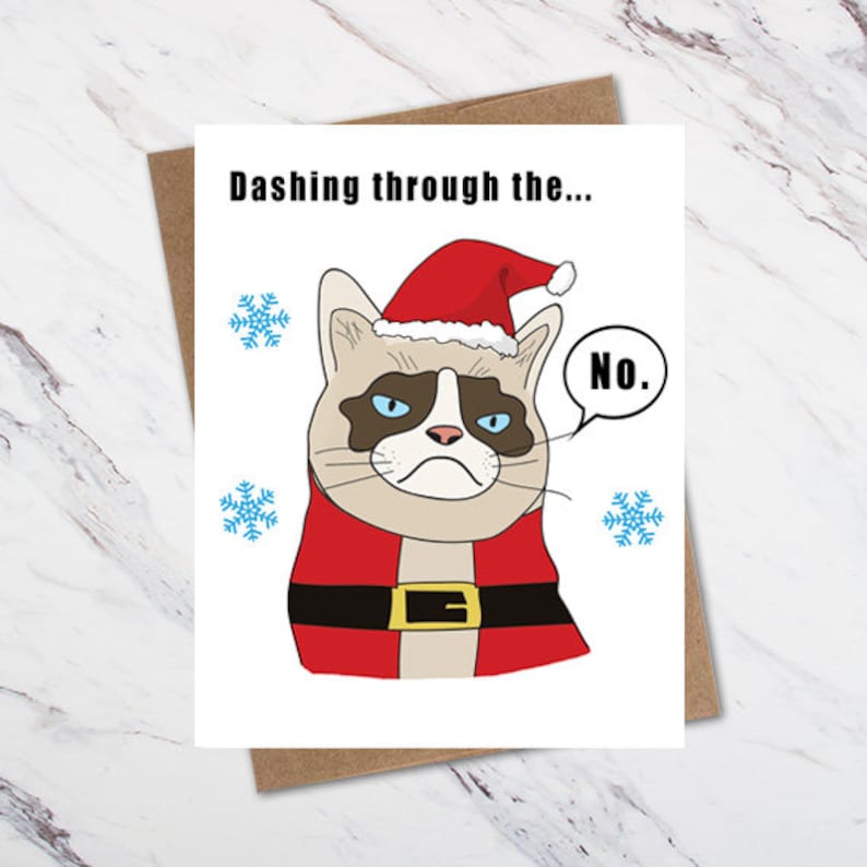 May include: A Christmas card featuring a grumpy cat wearing a Santa hat and a red and white Santa suit. The text on the card reads "Dashing through the... No."