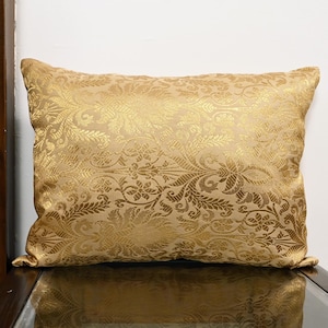 Puede incluir: Un cojín rectangular dorado con un estampado floral. El cojín tiene una superficie brillante y texturizada y está colocado sobre una superficie reflectante. El texto "CC-648" está en la esquina superior derecha.