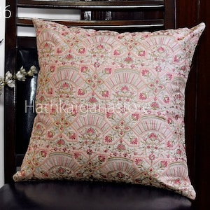 Puede incluir: Una almohada rosa y dorada con un patrón floral. La almohada está sentada en una silla marrón.