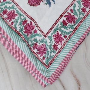 May include: Close-up of a white fabric with a pink and green floral print. The fabric is folded in layers, showing the pattern repeating. The fabric has a striped border in pink and green.