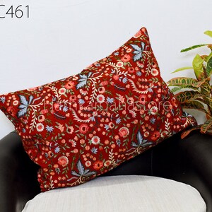 Puede incluir: Una almohada roja con un patrón de bordado floral. La almohada está en una silla negra y blanca.