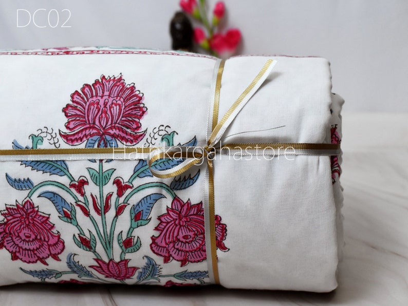 May include: A white cotton quilt with a floral print in shades of pink, blue, and green. The quilt is folded and tied with a gold ribbon. The text "DC02" is visible in the top left corner of the image.
