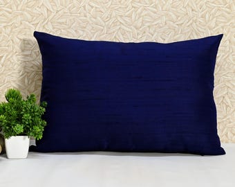 May include: A navy blue rectangular pillow with a smooth, textured fabric. The pillow is sitting on a white surface with a beige background.