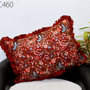 Puede incluir: Una almohada roja con un diseño bordado floral y un borde con volantes. La almohada está sentada en una silla negra.