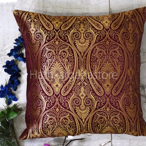 Pode incluir: Uma almofada de cor bordô e dourada com um padrão paisley. A almofada é feita de um tecido macio e luxuoso e é perfeita para adicionar um toque de elegância a qualquer ambiente.
