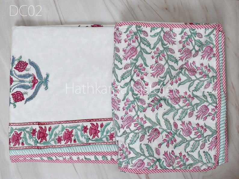 May include: A white cotton bed sheet with a pink and green floral print. The sheet has a red and white striped border and a single large floral design in the top left corner. The sheet is labeled "DC02".