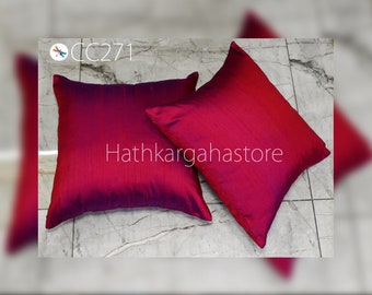Op de afbeelding: Twee vierkante kussenslopen met een diep rood en paars ombre-effect. De kussenslopen zijn gemaakt van een zijdeachtige stof en hebben een subtiele glans. De kussenslopen zijn gerangschikt op een betegelde ondergrond. De tekst "Hathkargahastore" is zichtbaar in het midden van de afbeelding.