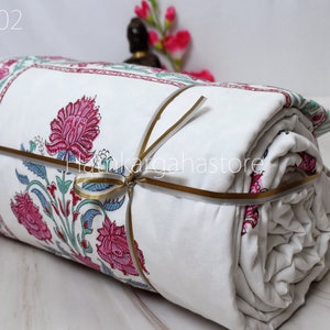 May include: A white cotton quilt with a floral print in shades of pink, green, and blue. The quilt is rolled up and tied with a gold ribbon. The text "DC02" is visible in the top left corner of the image.