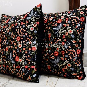 May include: Two black velvet pillow covers with embroidered floral designs in shades of pink, red, blue, and green. The pillows are square and have a black border.