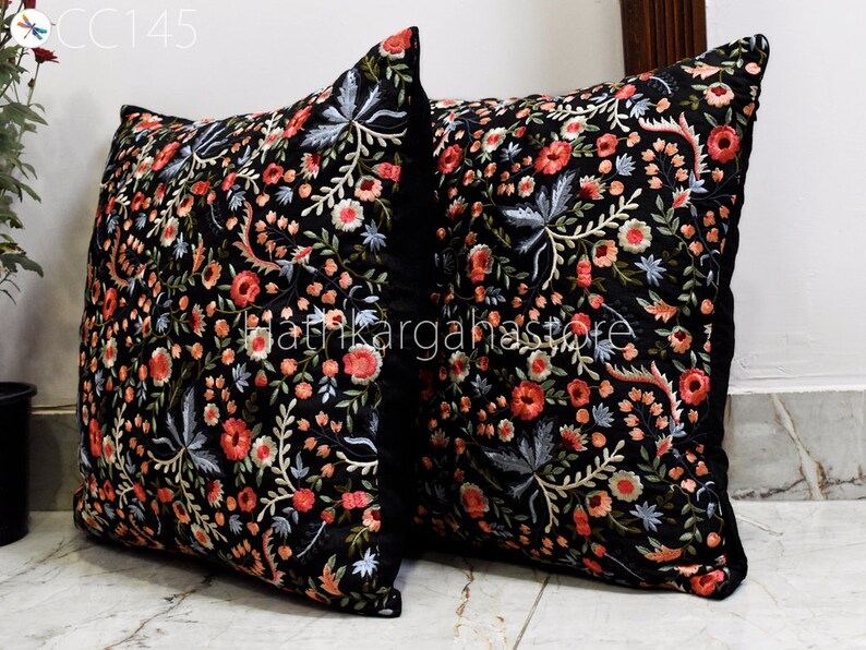 May include: Two black velvet pillow covers with embroidered floral designs in shades of pink, red, blue, and green. The pillows are square and have a black border.