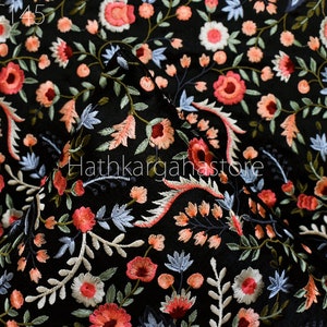 May include: Black fabric with a floral embroidery pattern in shades of pink, white, and blue. The fabric is shown folded in half, with the embroidery visible on both sides.