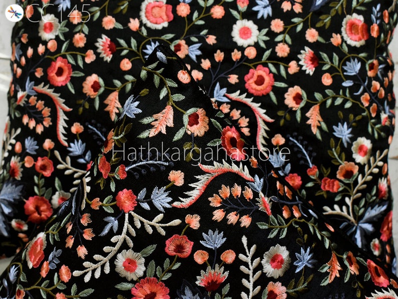 May include: Black fabric with a floral embroidery pattern in shades of pink, white, and blue. The fabric is shown folded in half, with the embroidery visible on both sides.