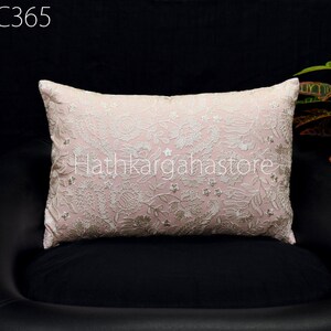 Puede incluir: Una almohada rosa con bordado floral blanco. La almohada está en una silla de cuero negro.