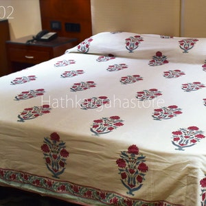 May include: A white cotton bed sheet with a red and blue floral print. The sheet has a border with a repeating pattern of red and blue flowers. The text "Hathkhagahastore" is visible in the center of the sheet.