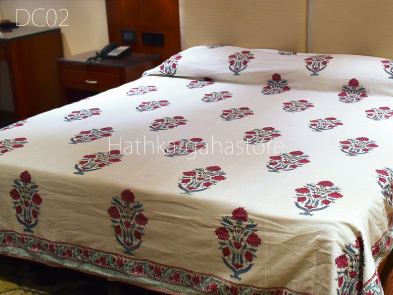 May include: A white cotton bed sheet with a red and blue floral print. The sheet has a border with a repeating pattern of red and blue flowers. The text "Hathkhagahastore" is visible in the center of the sheet.