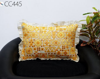 May include: A yellow and white throw pillow with a geometric pattern and mirror embellishments. The pillow has a ruffled edge and is sitting on a black couch.