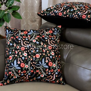 May include: Two black throw pillows with a floral embroidery pattern in shades of pink, white, and blue. The pillows are on a gray couch.
