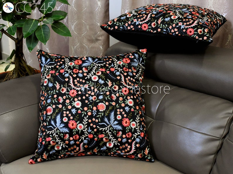 May include: Two black throw pillows with a floral embroidery pattern in shades of pink, white, and blue. The pillows are on a gray couch.