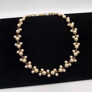 May include: A delicate gold chain necklace with a cluster of faux pearls in a cascading design. The pearls are off-white and the chain is a light gold color.
