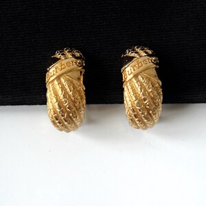 May include: A pair of gold-tone hoop earrings with a rope-like design and the word "Burberry" engraved on each earring.